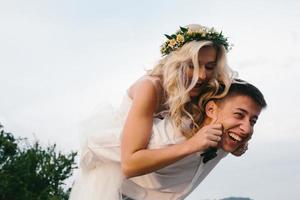 sposo trasporta sposa su il suo indietro all'aperto foto