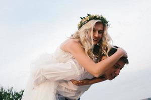 sposo trasporta sposa su il suo indietro all'aperto foto