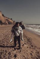 uomo trasporta il suo fidanzata su Indietro, coppia avendo divertimento su il riva del mare foto