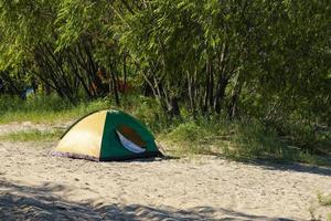 turista tenda su il sabbioso banca di il fiume, contro il fondale di verde vegetazione. foto