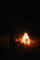 donna seduta e ottenere caldo vicino il falò nel il notte foresta. foto