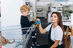 bellissimo madre trasporta sua poco figlio nel il supermercato carrello foto