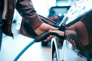 la mano umana sta tenendo la ricarica dell'auto elettrica collegata all'auto elettrica foto