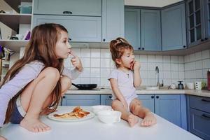 Due poco ragazze nel il cucina seduta su il tavolo. foto