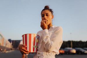 giovane carino donna Tenere Popcorn nel un' shopping centro commerciale parcheggio lotto foto