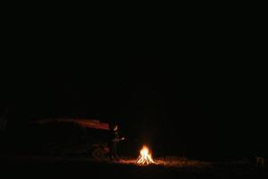 donna seduta e ottenere caldo vicino il falò nel il notte foresta. foto