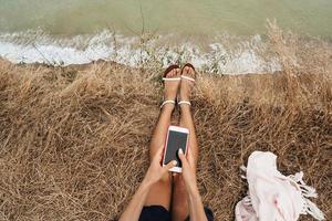 bellissimo giovane ragazza seduta e Tenere un' smartphone nel sua mani, superiore Visualizza foto