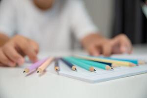 ragazzo persona seduta studia interno a casa, maschio ragazzo alunno in linea apprendimento e fare compiti a casa su scrivania, giovane bambino lettura e scrittura un' libro su tavolo. concetto di formazione scolastica, tecnologia cyberspazio foto