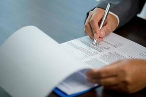 posto di lavoro avvicinamento persona professionale donna d'affari seduta a scrivania hold penna firma o firma contrarre carta. dipendente donna scrittura accordo documento su lavoro d'ufficio modulo aziendale a opera ufficio foto