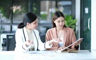 due giovani donne d'affari asiatiche discutono della strategia di lavoro e pianificazione del progetto di investimento. uomini d'affari che parlano insieme al computer portatile in ufficio. foto