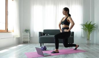 sorridente asiatico donna fare yoga spalla allungamento in linea classe a partire dal il computer portatile a casa nel vivente camera. se stesso solitudine e allenarsi a casa. foto