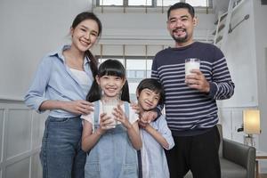 ritratto di contento salutare asiatico tailandese famiglia, poco figli, e giovane genitori con bicchiere di latte nel mattina, Sorridi e Guarda a telecamera insieme a bello casa, benessere nutrizione prima colazione stile di vita.