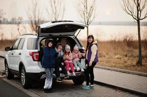 madre con quattro bambini seduti nel bagagliaio di una grande auto suv. foto