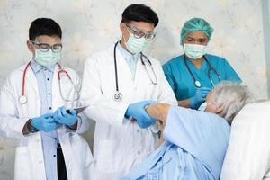 il team di medici asiatici controlla la vecchia paziente anziana per la malattia alla motivazione nuova normalità per il trattamento dell'infezione covid-19 coronavirus nel reparto ospedaliero. foto