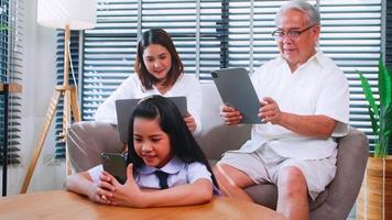 Nonno, madre e figlia uso senza fili tecnologia mentre rilassante nel il vivente camera. asiatico famiglia è godendo il moderno mobile tecnologia nel loro casa. foto