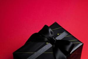 superiore Visualizza di nero regalo scatola con rosso e nero nastri isolato su rosso sfondo. foto