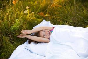 ragazza dorme su letto nel erba, dolce tratti e sbadiglia assonnato, bene mattina nel fresco aria. ecologico, salutare dormire, protezione a partire dal zanzare, pulito natura, ecologia, figli di Salute foto