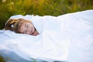 il ragazza dorme su bianca letto biancheria nel natura nel il erba, nel il fresco aria. protezione a partire dal zanzare, salutare dormire, il benefici di ventilazione, indurimento, pulito natura, ecologia, figli di Salute foto