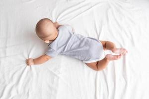 superiore Visualizza e bambino nel un' a strisce camicia è strisciando su un' bianca tappeto. foto