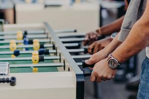 uomini irriconoscibili giocano a calcio balilla, si divertono con il gioco di squadra, vogliono vincere avversari, trascorrono il tempo libero al pub. gioco di kicker. partita di calcio balilla foto