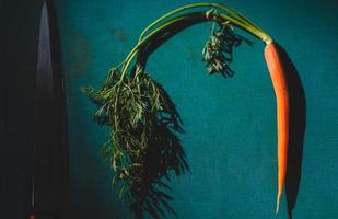 un' carota e chef coltello su il tavolo foto