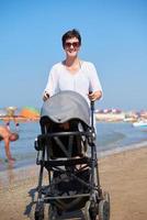 madre a piedi su spiaggia e spingere bambino carrozza foto