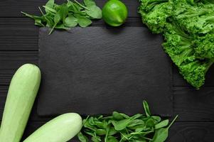 tavola di pietra nera su fondo di legno nero decorato con verdure ed erbe aromatiche. foto