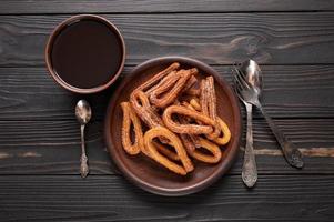 churros fatti in casa con cioccolato su fondo rustico di legno scuro. foto