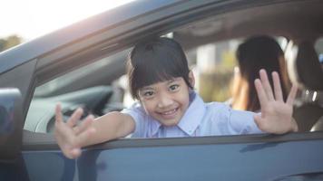 asiatico alunno ragazza pronto per partire per scuola e agitando addio o dire Ciao su auto sfondo. indietro per scuola concetto. foto