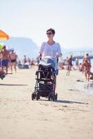 madre a piedi su spiaggia e spingere bambino carrozza foto