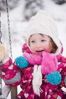 poco ragazza a nevoso inverno giorno swing nel parco foto