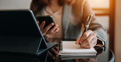 mano della donna di affari che lavora con il nuovo computer moderno e che scrive sul diagramma di strategia del blocco note come luce del mattino di concetto foto