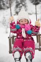 poco ragazza a nevoso inverno giorno swing nel parco foto
