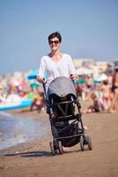 madre a piedi su spiaggia e spingere bambino carrozza foto