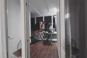 uomo Ciclismo su il macchina allenatore lui è esercizio nel il casa a notte giocando in linea bicicletta da corsa gioco foto