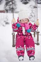 poco ragazza a nevoso inverno giorno swing nel parco foto