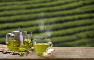 verde tè tazza e bicchiere brocche o barattoli. con e verde tè foglia licenziamento su il di legno tavolo e il tè piantagioni sfondo foto