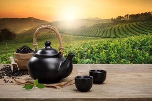 tazza di caldo tè con teiera, verde tè le foglie e secco erbe aromatiche su il di legno tavolo nel piantagioni sfondo con vuoto spazio, biologico Prodotto a partire dal il natura per salutare con tradizionale foto