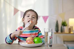 bambino asiatico ragazza mangiare Mela su il scrivania, salutare cibo abitudini concetto foto