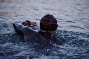 atleta di triathlon che nuota sul lago all'alba indossando la muta foto