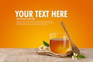 miele ape nel bicchiere vaso con miele mestolo e fiori su il di legno tavolo, arancia sfondo a con copia spazio per il tuo testo. foto