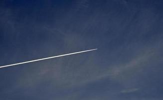 un' aereo volante nel il blu cielo e nuvole. un' bianca scia di condensazione a partire dal un aereo nel il estate cielo. foto