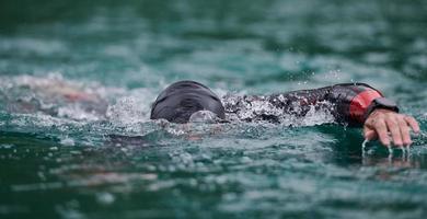 atleta di triathlon che nuota sul lago indossando la muta foto