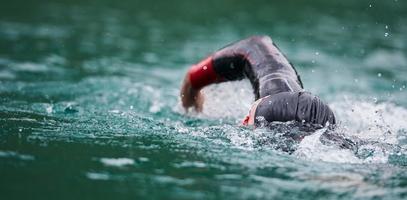 atleta di triathlon che nuota sul lago indossando la muta foto