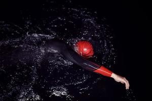 atleta di triathlon che nuota nella notte buia che indossa la muta foto