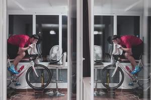 uomo Ciclismo su il macchina allenatore lui è esercizio nel il casa a notte giocando in linea bicicletta da corsa gioco foto