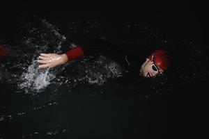 atleta di triathlon che nuota nella notte buia che indossa la muta foto