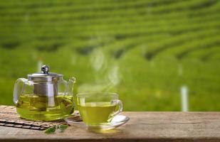 verde tè tazza e bicchiere brocche o barattoli. con e verde tè foglia licenziamento su il di legno tavolo e il tè piantagioni sfondo foto