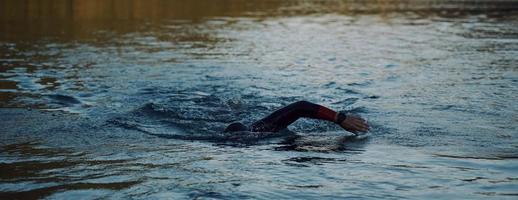 atleta di triathlon che nuota sul lago all'alba indossando la muta foto