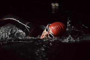 atleta di triathlon che nuota nella notte buia che indossa la muta foto